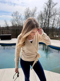 Woman in a beige cardigan standing by a pool with trees and a cloudy sky in the background