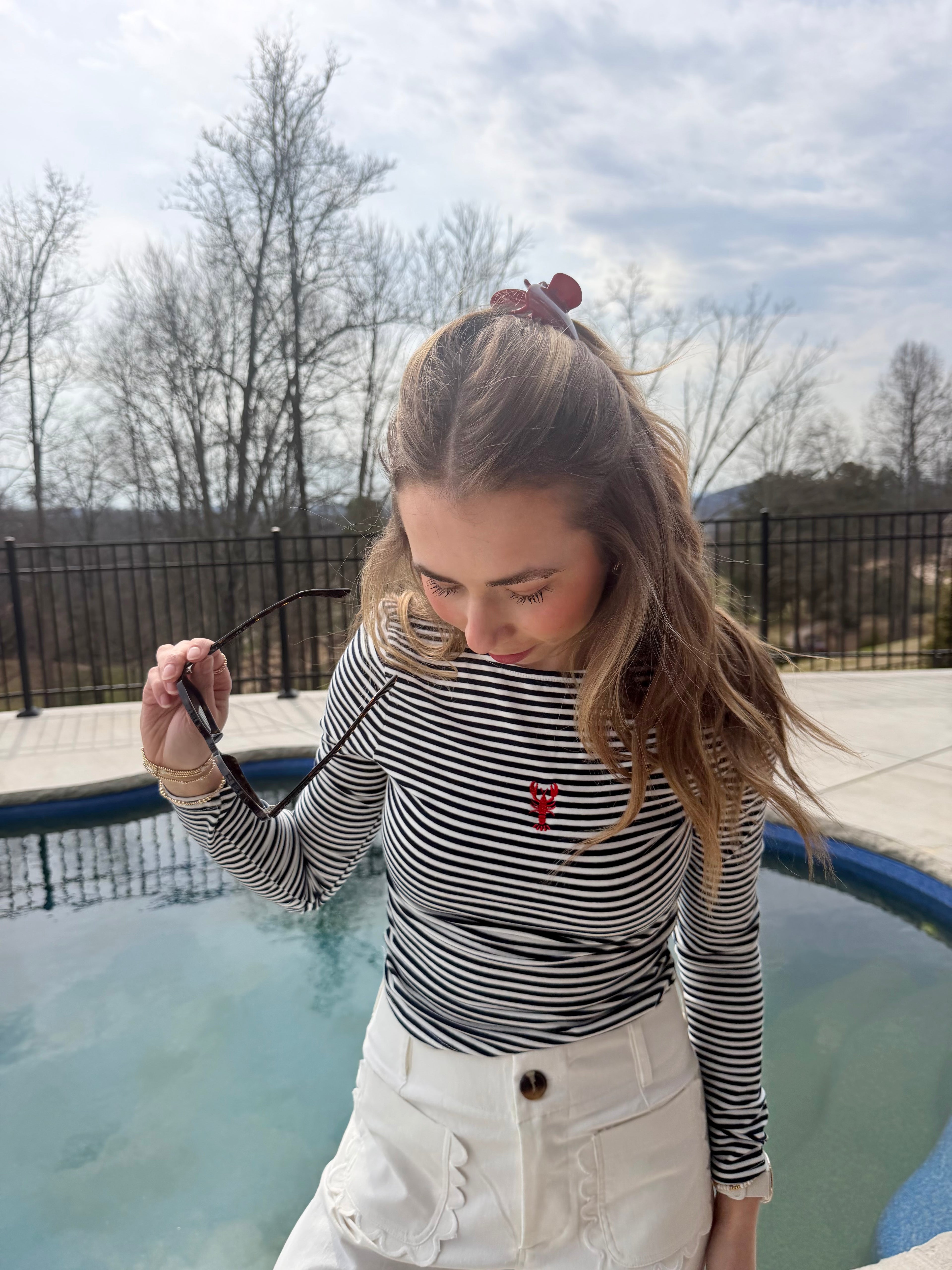 Women in a navy striped tee with a red lobster standing in front of a pool. 