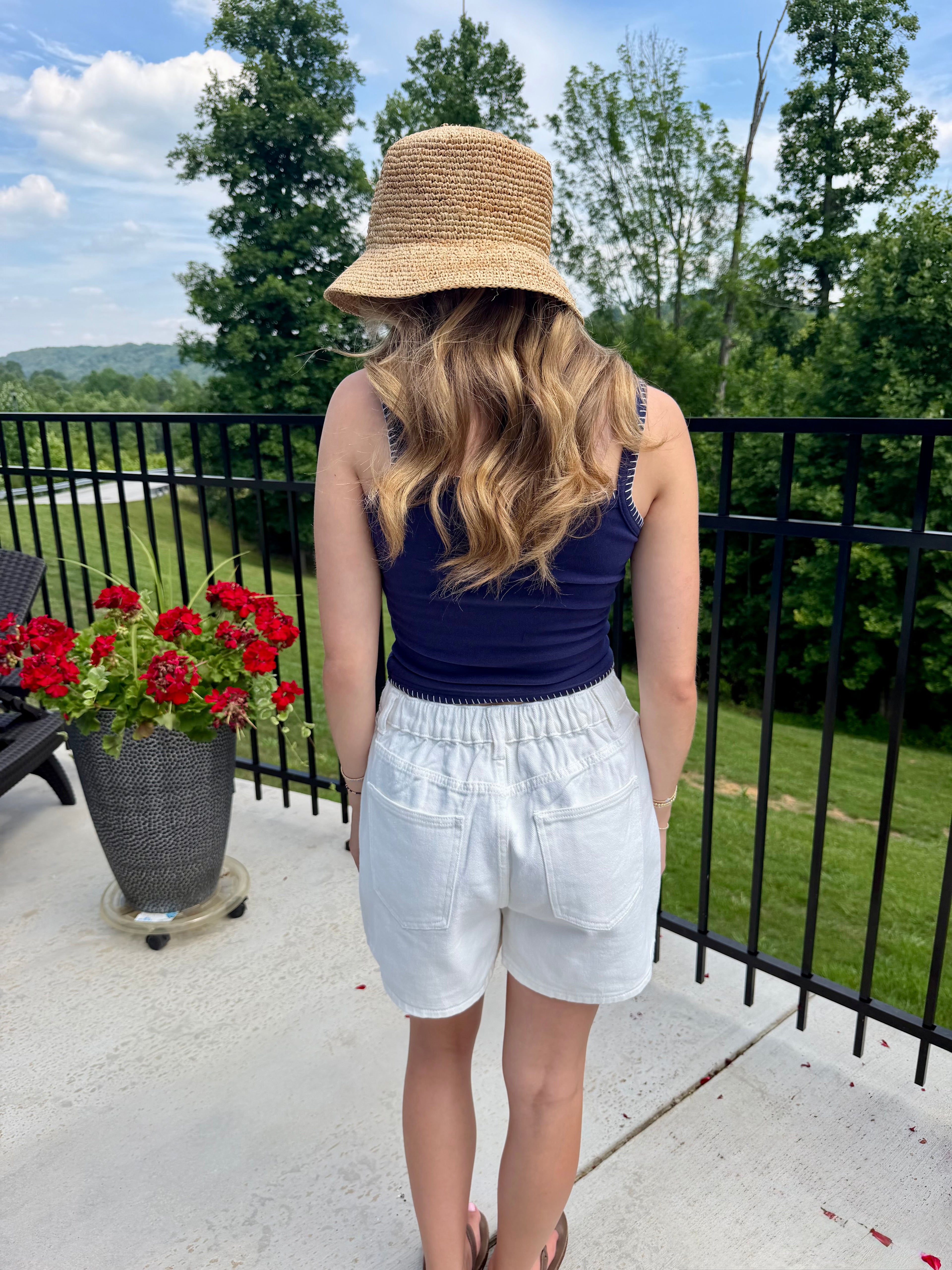 Person wearing a straw hat and blue top on a balcony with greenery