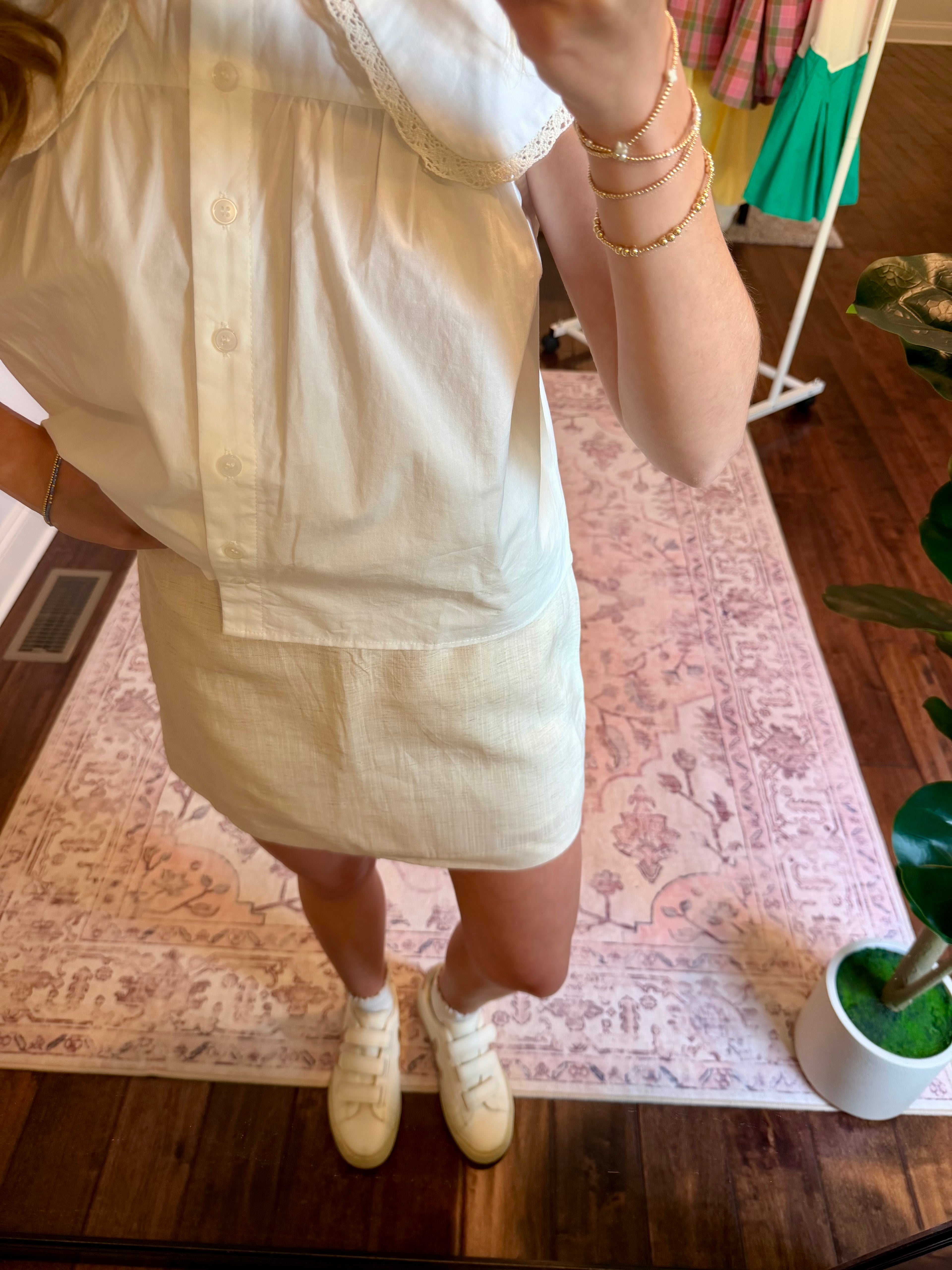 Person wearing a cream skirt and white top with a patterned rug and wooden floor in the background