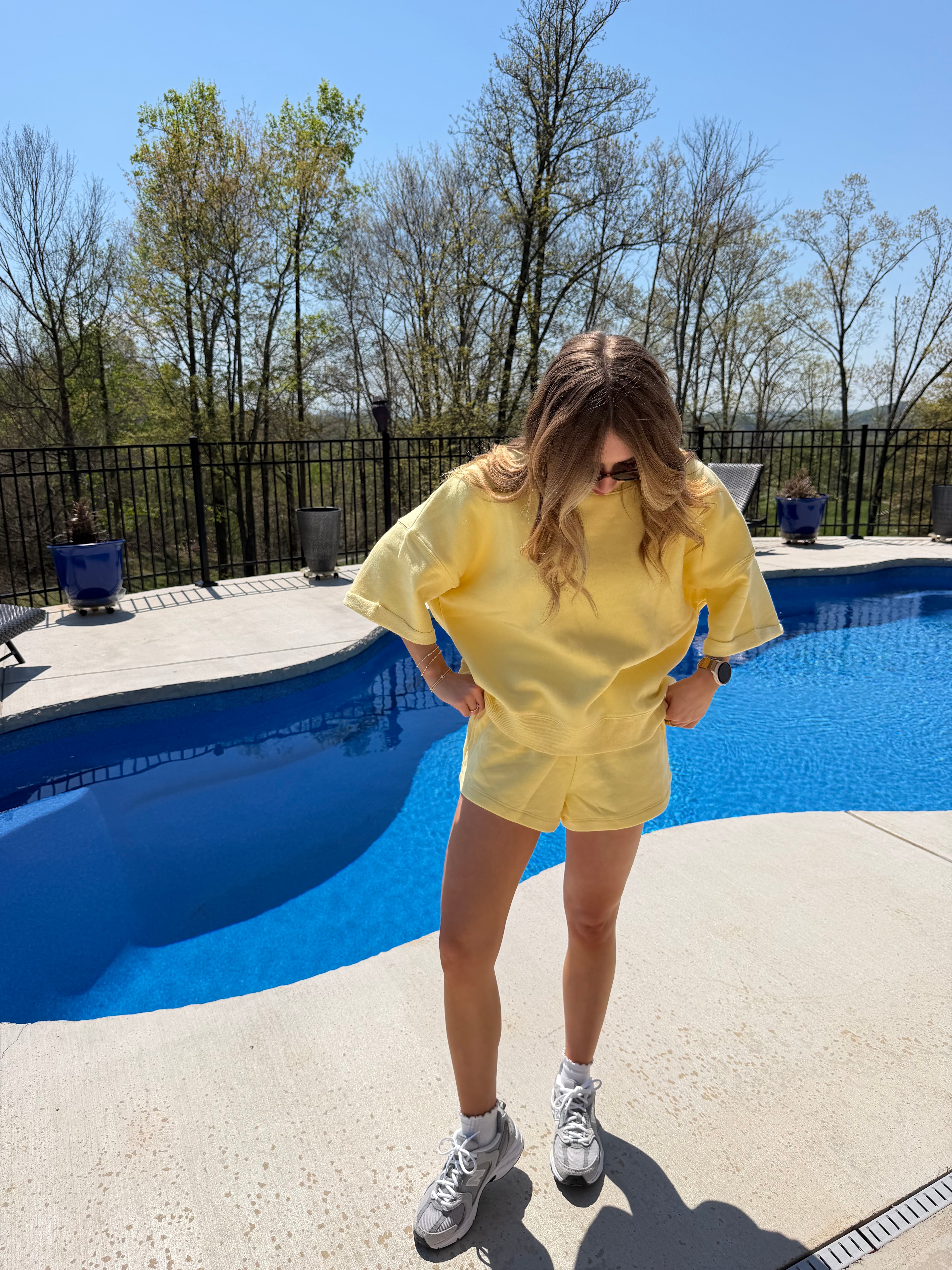Person in a yellow set standing by a blue pool on a sunny day.
