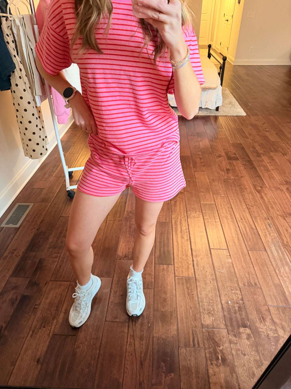 Person taking a mirror selfie wearing a pink matching set in a room with wooden floor and white walls.