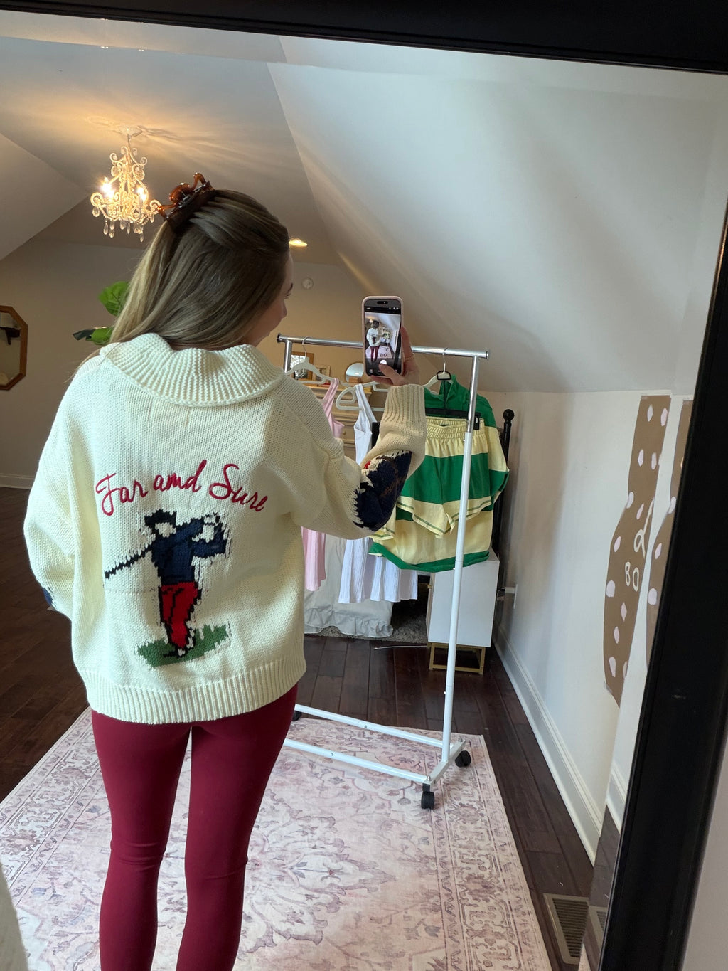 Person wearing a white sweater with green and red patterns, standing on a patterned rug.