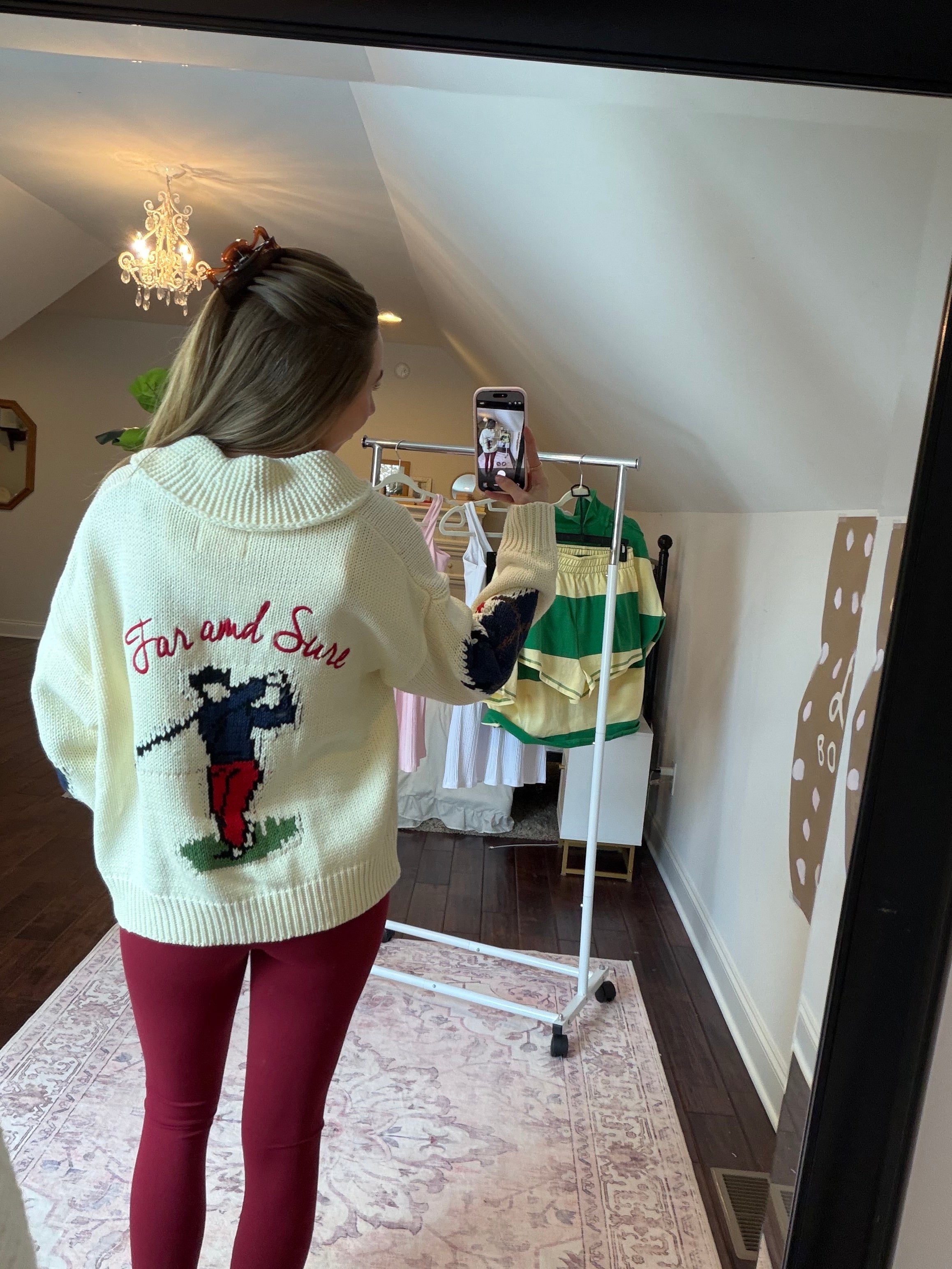 Person wearing a white sweater with green and red patterns, standing on a patterned rug.