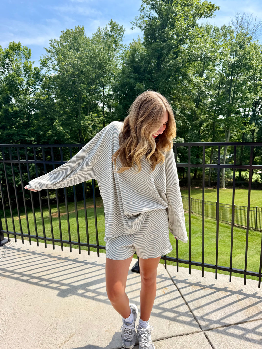 Woman in a light gray outfit standing on a sidewalk with trees in the background
