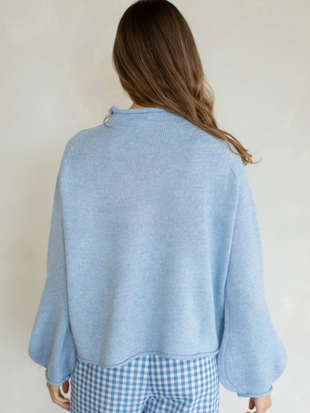 Person wearing a light blue sweater over a checkered outfit against a plain background