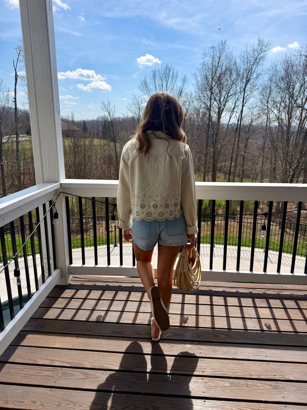 Woman standing on a wooden deck overlooking a scenic landscape with bare trees and a clear blue sky.