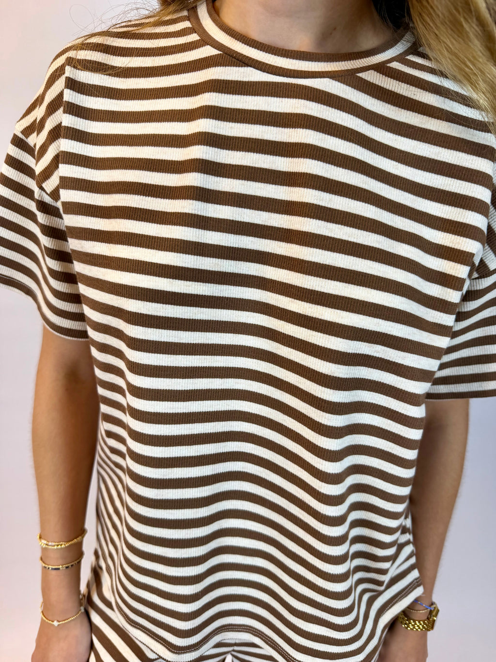 A close-up of a person wearing a short-sleeve ribbed knit top with horizontal brown and off-white stripes.