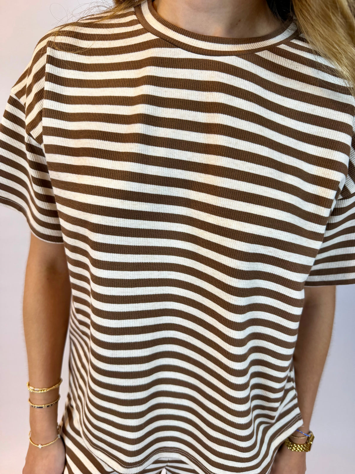 A close-up of a person wearing a short-sleeve ribbed knit top with horizontal brown and off-white stripes.