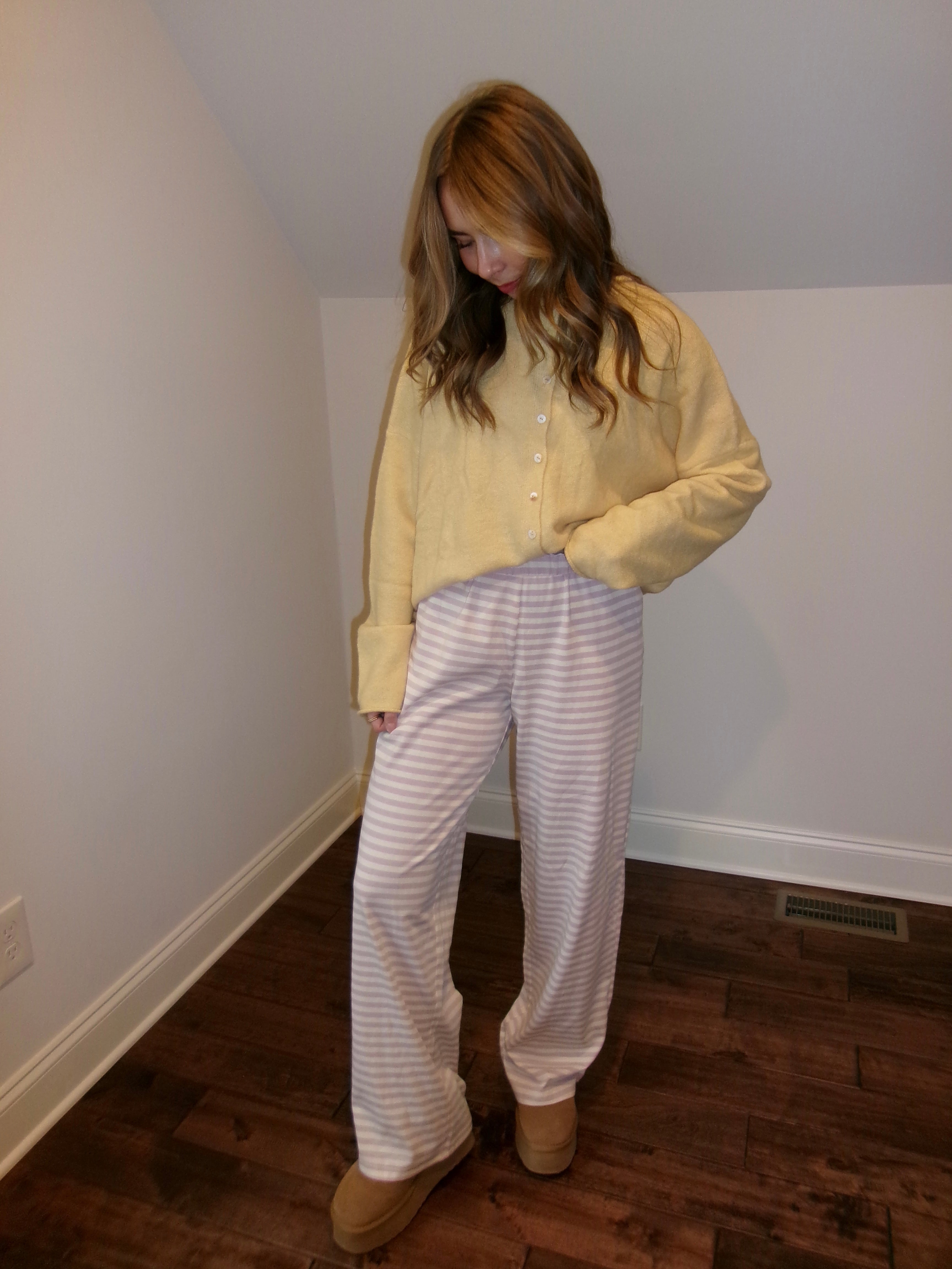 Person wearing a yellow shirt and white striped pants in a room with wooden flooring.