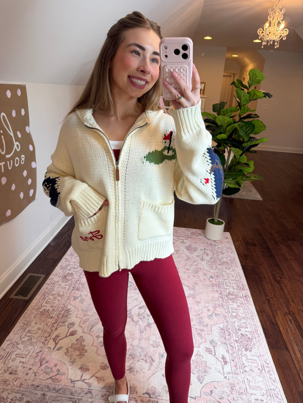 Person wearing a white sweater with green and red patterns, standing on a patterned rug.