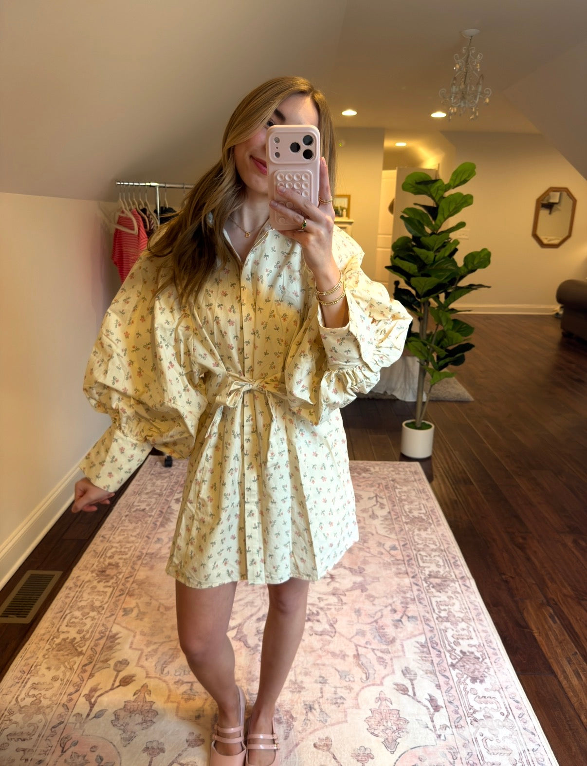 Woman in a floral dress standing on a patterned rug in a room with a plant and furniture.