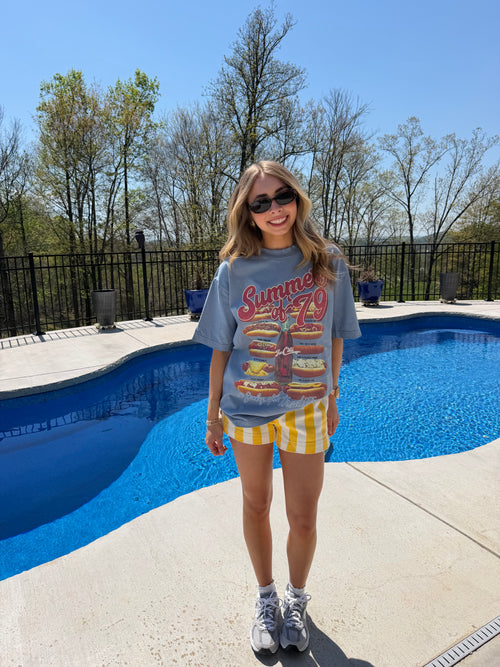 Person standing by a pool wearing sunglasses and a graphic t-shirt.