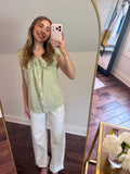 Woman taking a mirror selfie wearing a green checkered top and white pants.