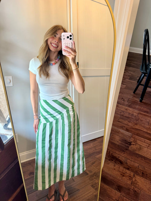 Woman taking a mirror selfie wearing a white top and green striped skirt.