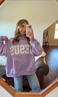 Person wearing a purple sweatshirt with 'JESUS' printed on it, taking a mirror selfie.