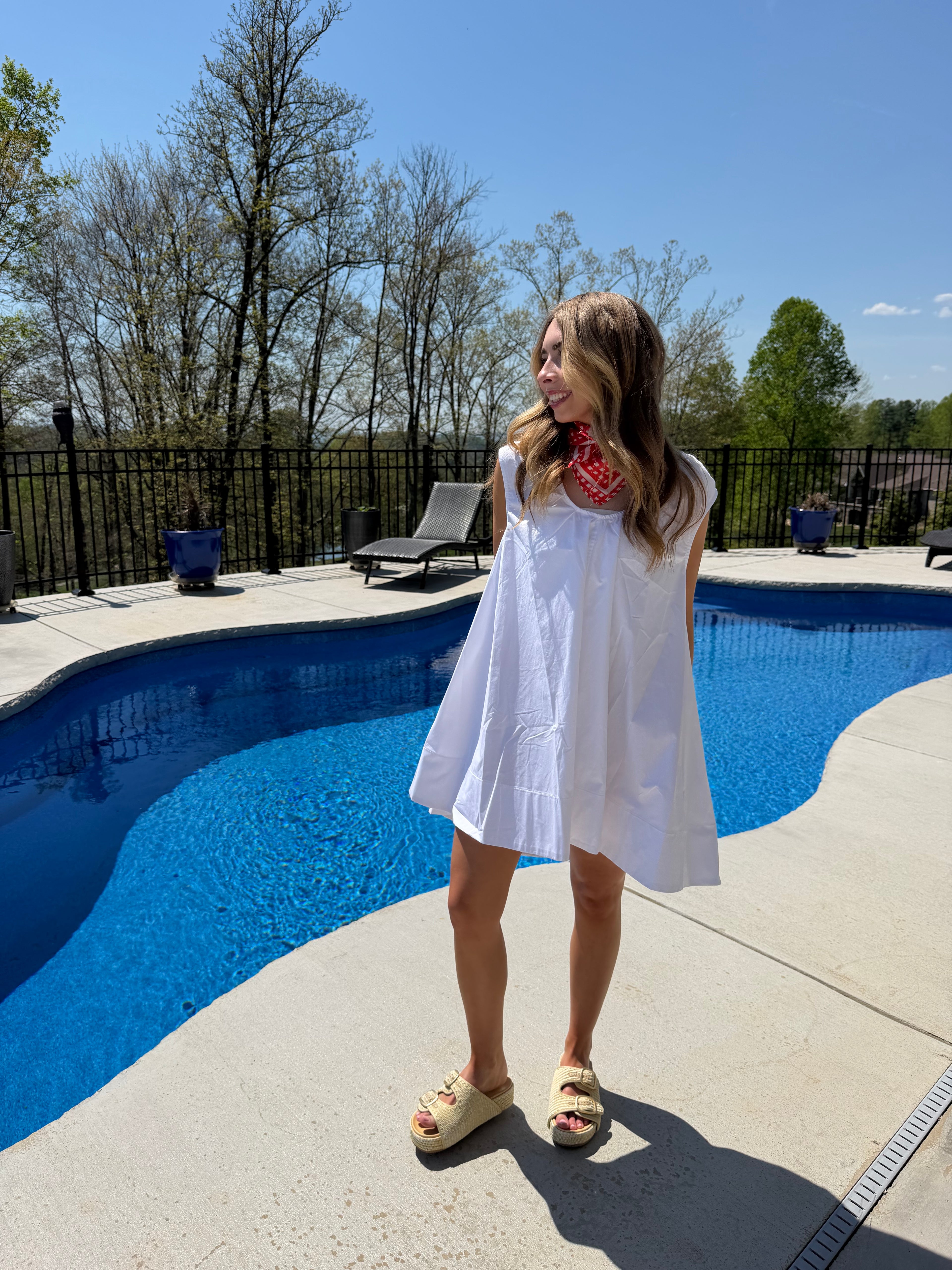 Woman in a white dress standing by a pool with a clear blue sky.