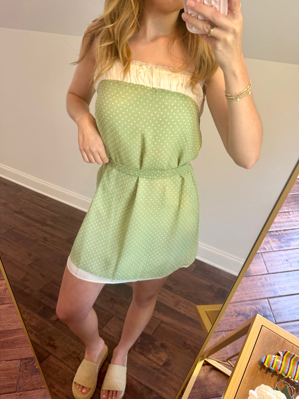 Woman wearing a green strapless dress with a white lace top, standing in front of a mirror.