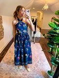 Woman taking a mirror selfie wearing a blue floral dress  in a room with a plant and decorative wall art.