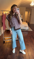 Person taking a mirror selfie wearing a pink and brown striped sweater vest and jeans in a bedroom.