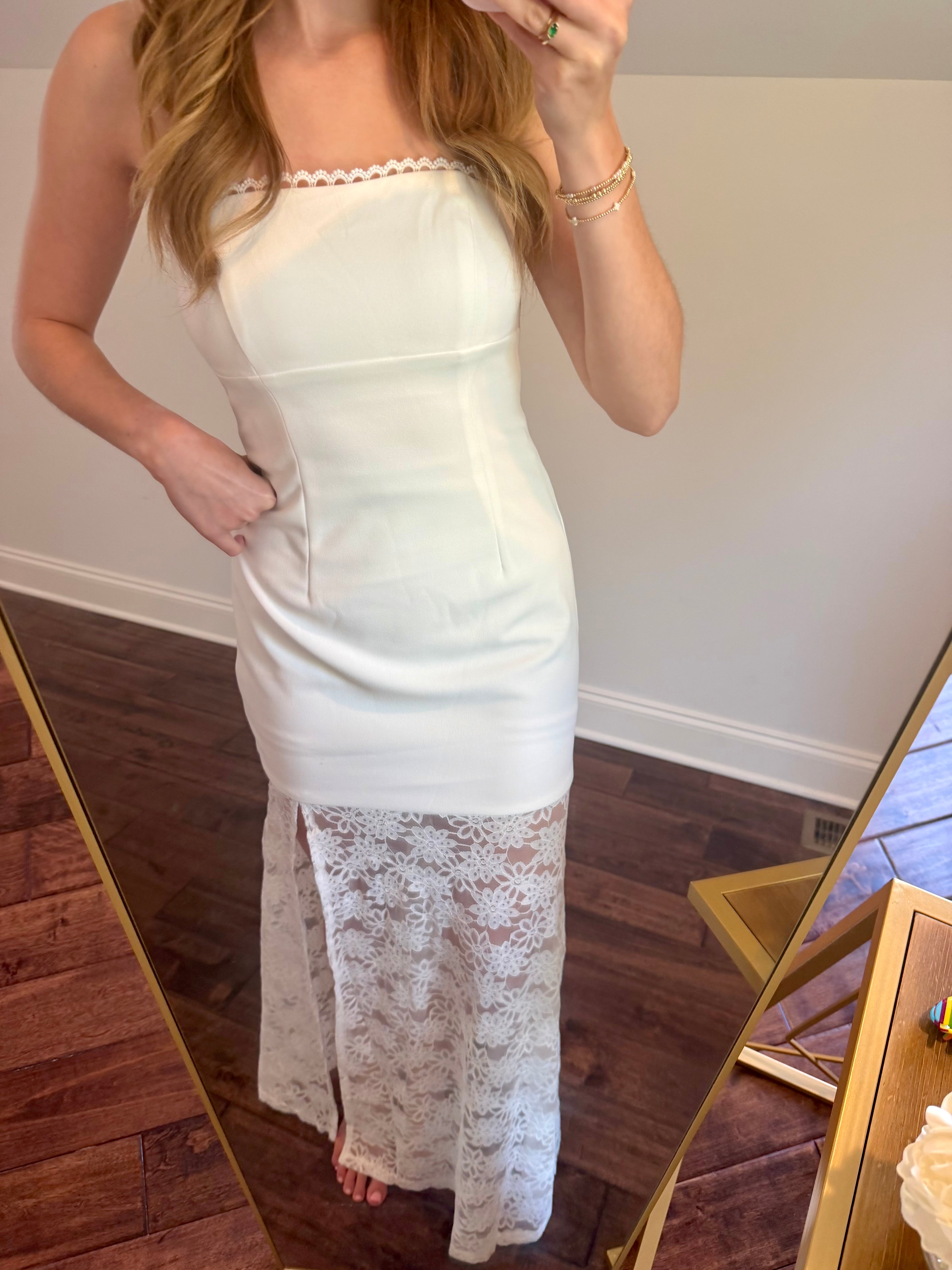 Person wearing a white strapless dress with lace detailing in a room.