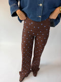 A person wearing brown wide-leg pants with light blue polka dots, styled with a blue denim jacket and brown shoes against a plain white studio background.