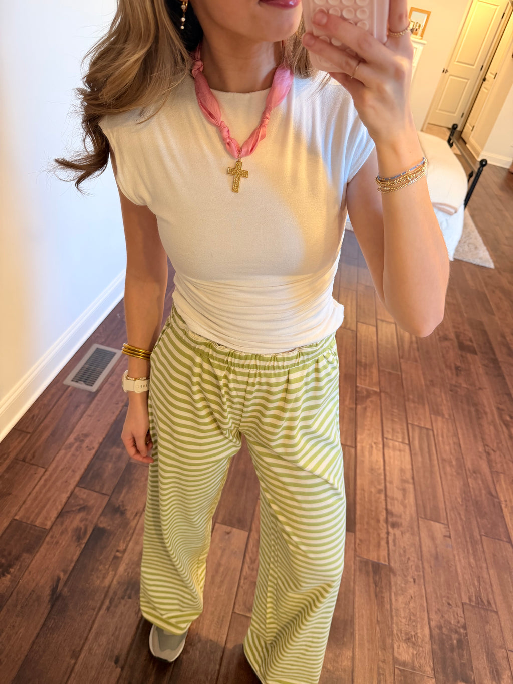 Person wearing a white top and green striped pants on a wooden floor.