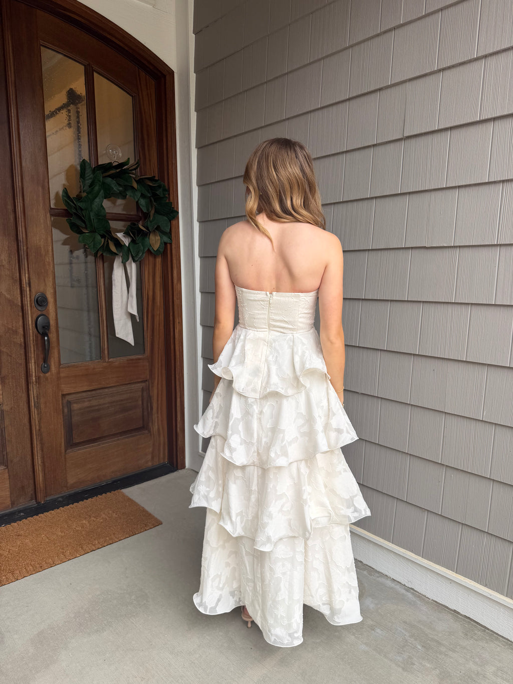 Woman in a white dress standing in front of a wooden door with a wreath.