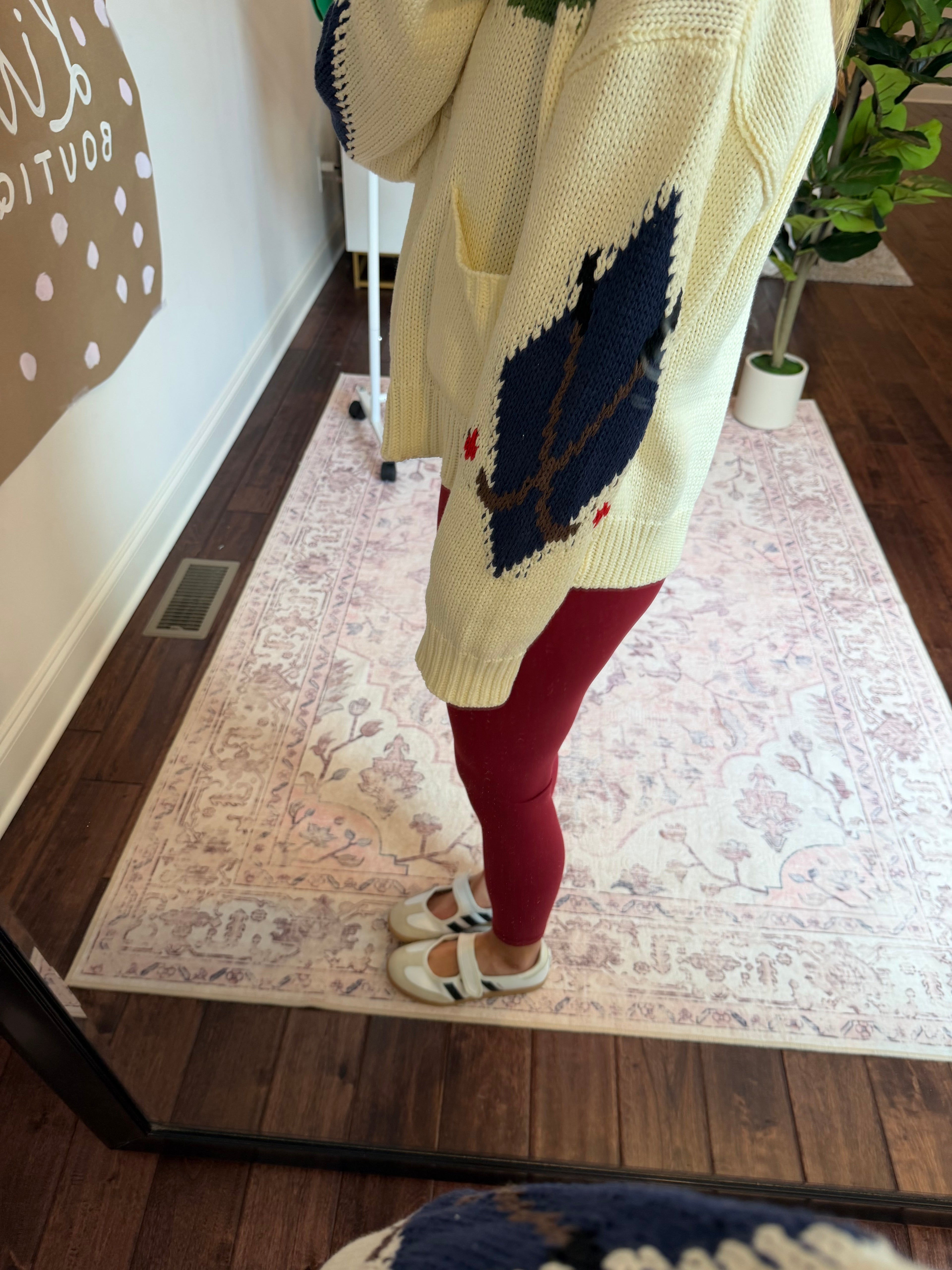 Person wearing a white sweater with green and red patterns, standing on a patterned rug.