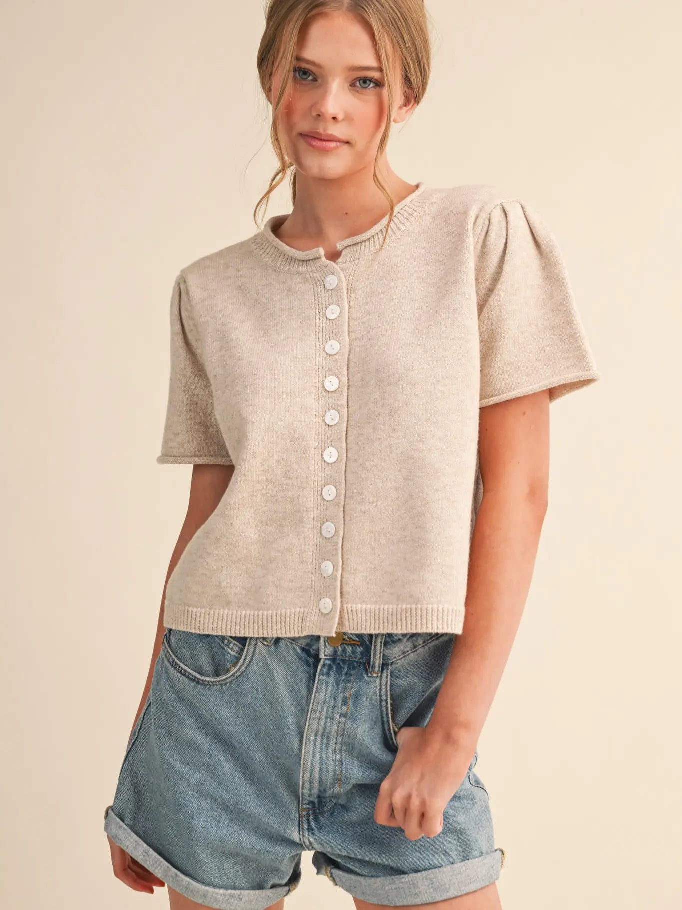 Woman wearing a beige short-sleeve cardigan and denim shorts on a beige background