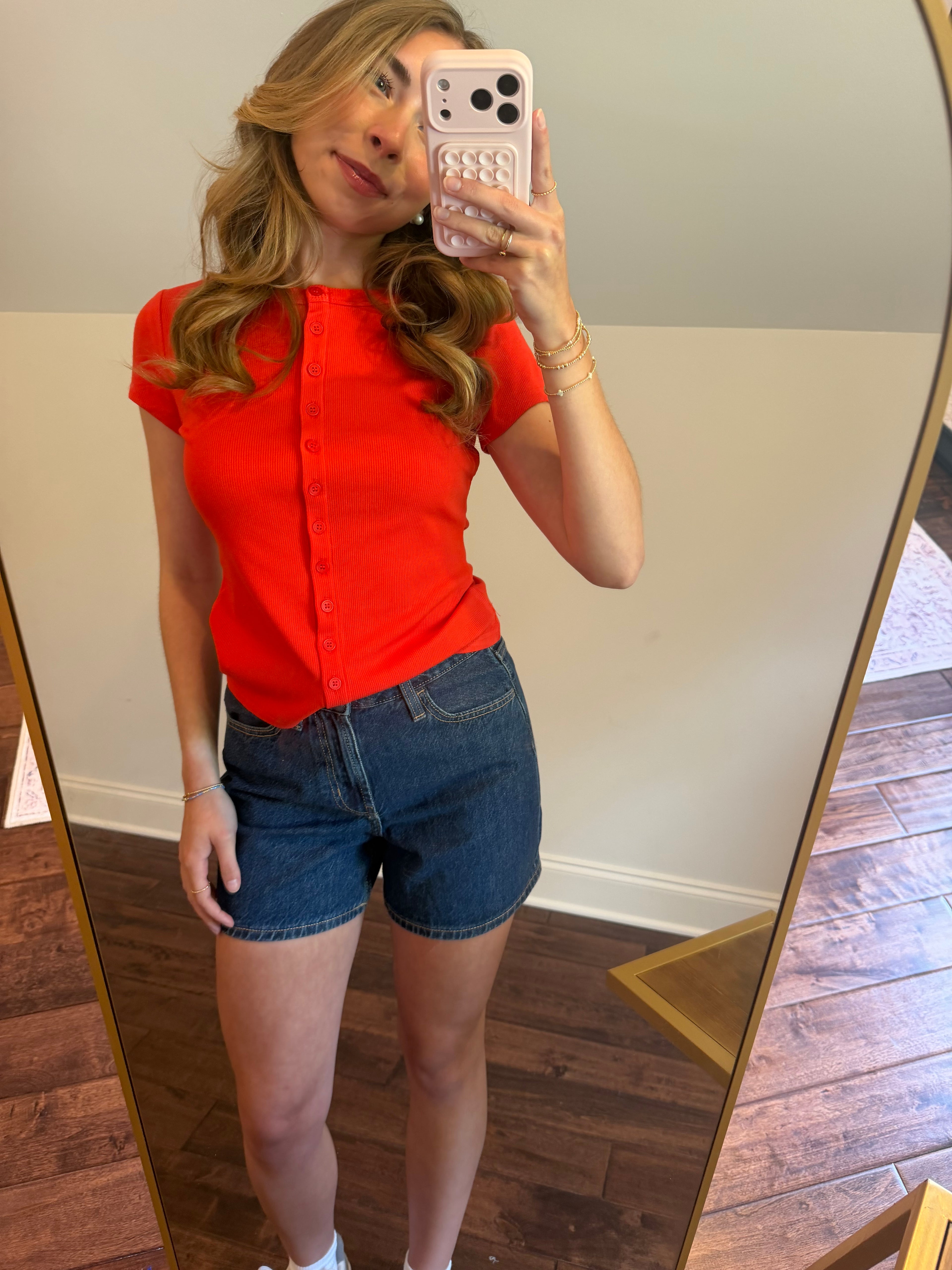 Person wearing a red shirt and denim shorts taking a mirror selfie.
