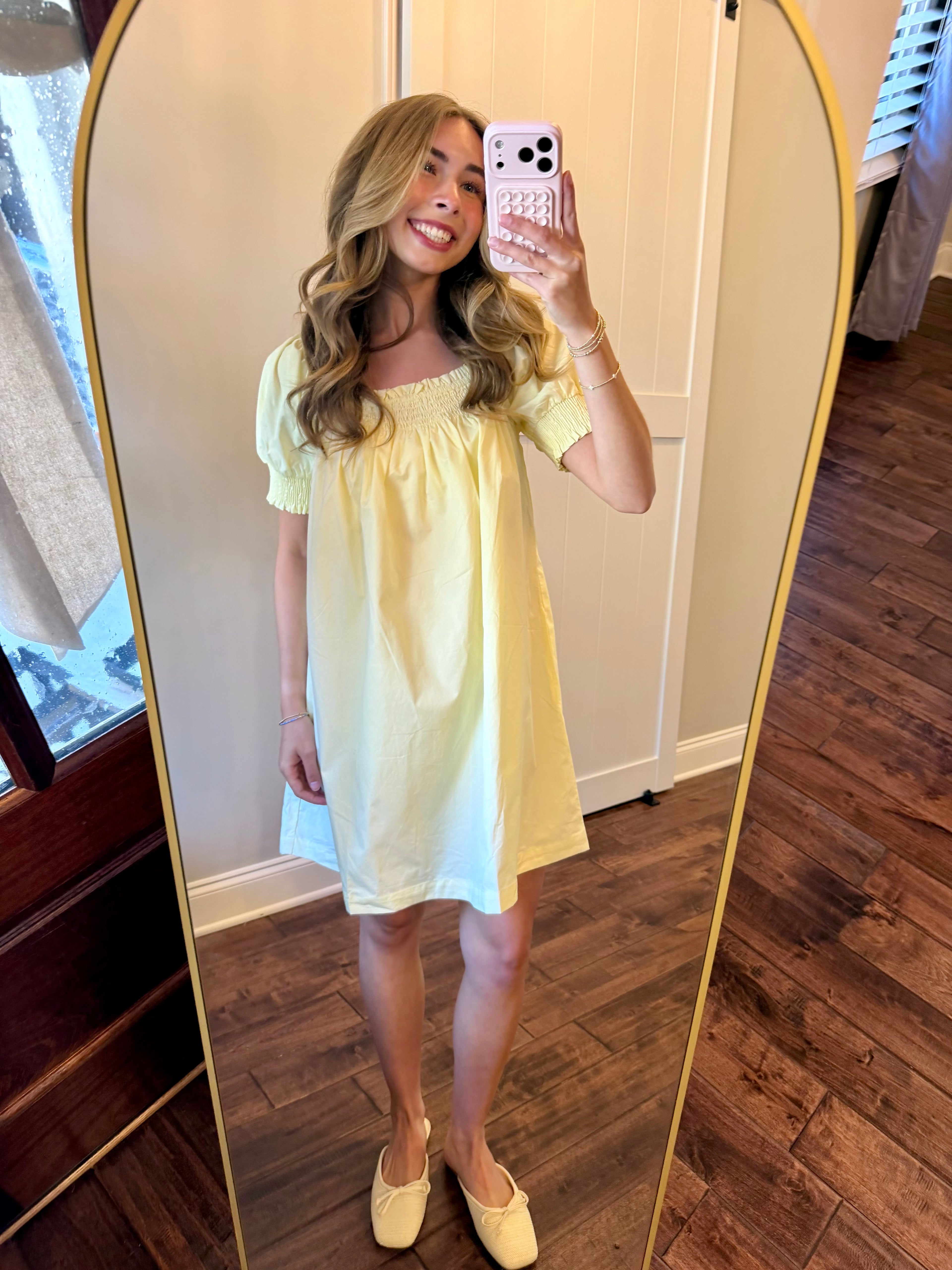 Woman taking a mirror selfie wearing a yellow dress in a room with wooden flooring.