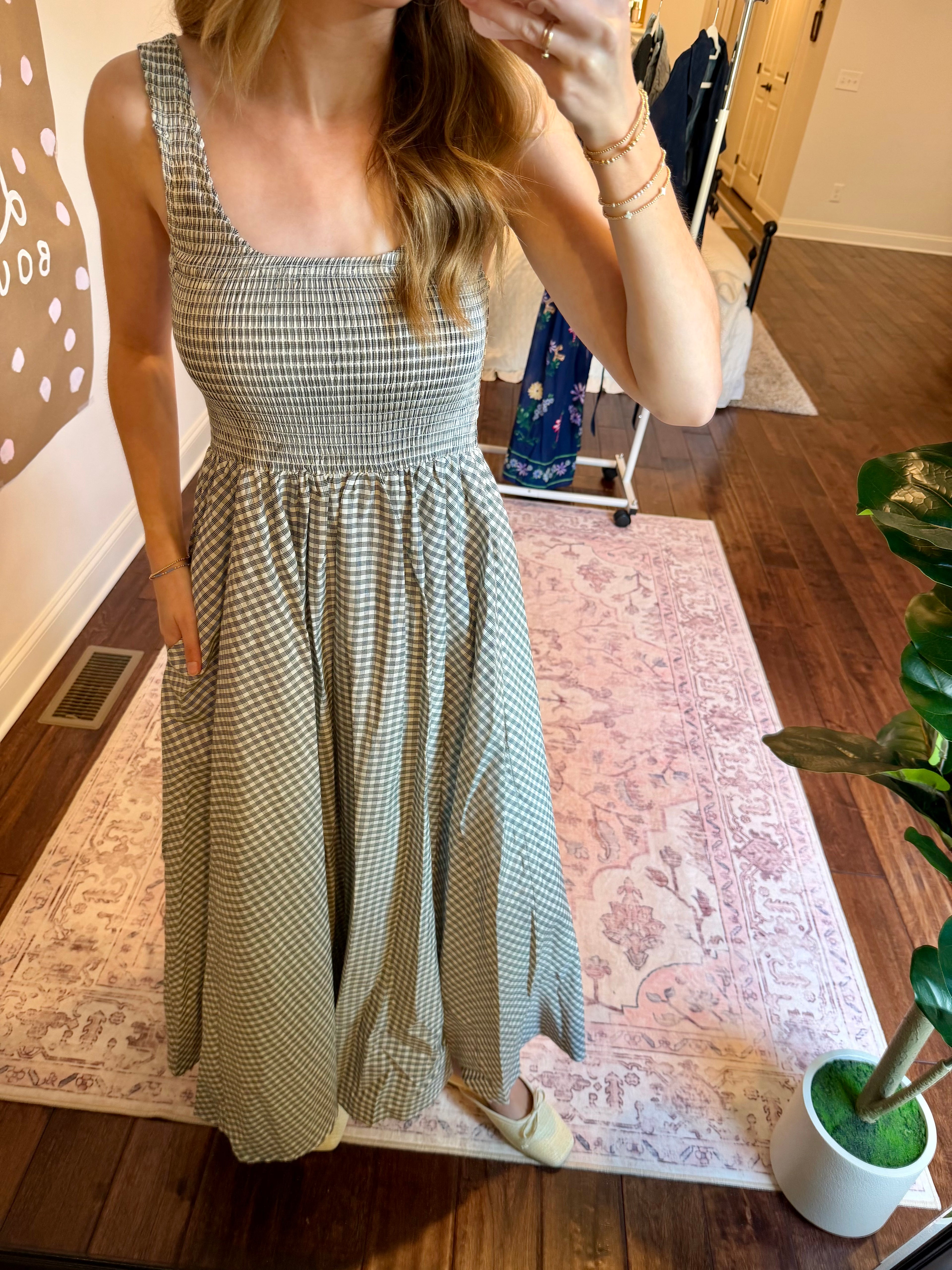 Woman taking a mirror selfie wearing a checkered dress in a home setting.