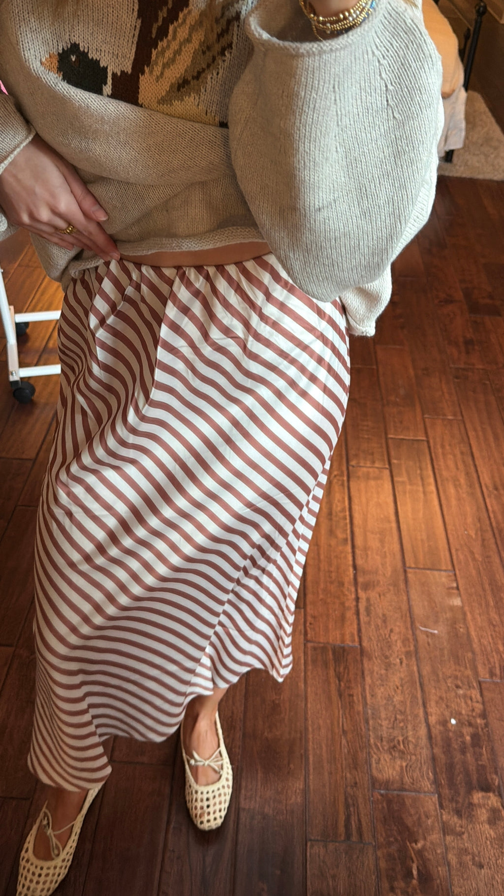 Person wearing a white sweater with a duck design and a brown and white striped skirt indoors.