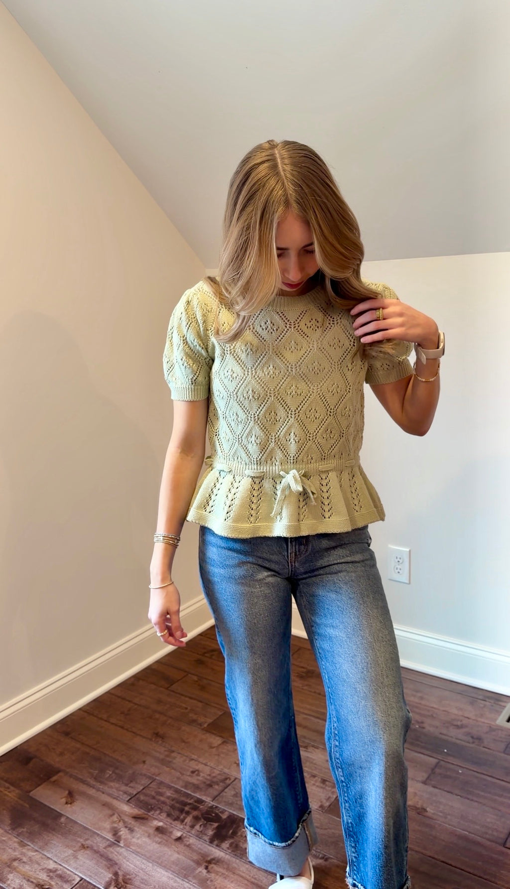 Woman wearing a green knitted top and blue jeans indoors.