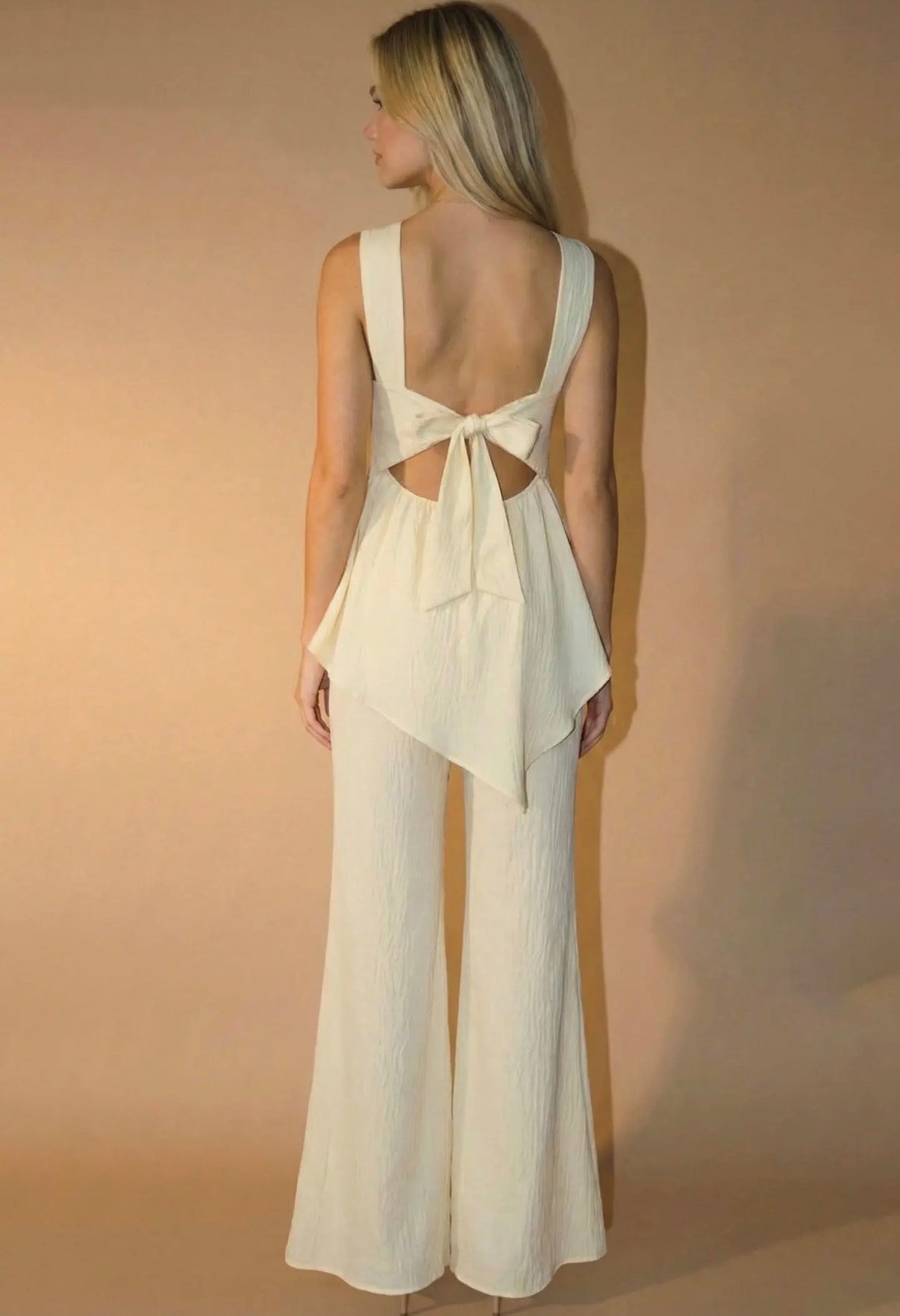 Woman wearing a white jumpsuit with cut-out back design against a beige background