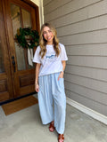 Woman standing outside a house wearing a white t-shirt and light blue pants.