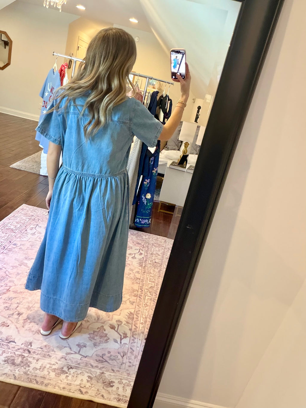 Woman taking a mirror selfie wearing a blue dress in a store.