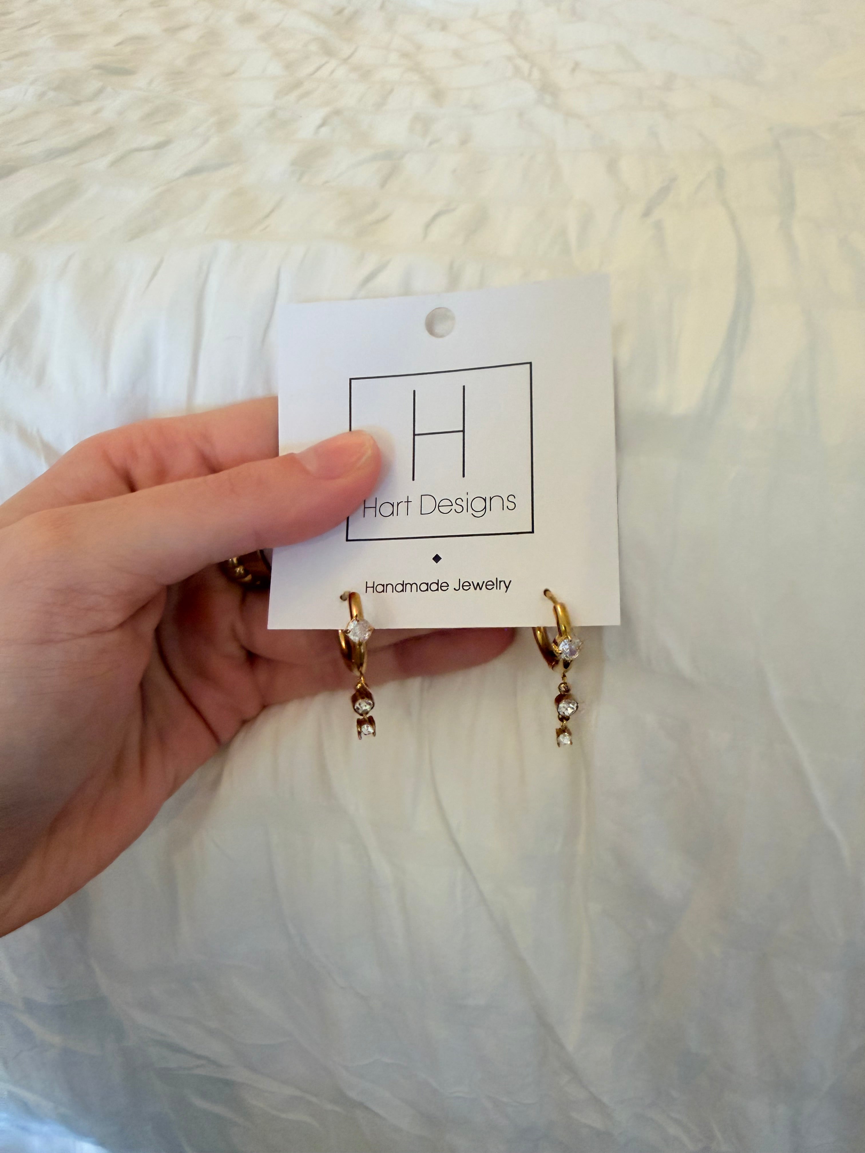 Hand holding a pair of gold earrings with a white card on a textured white background