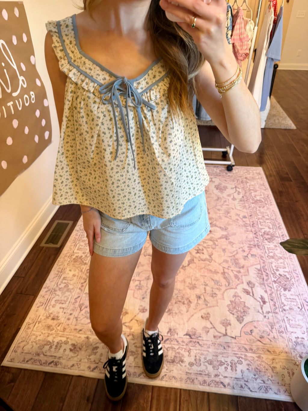 Person wearing a floral top and denim shorts in a home setting.