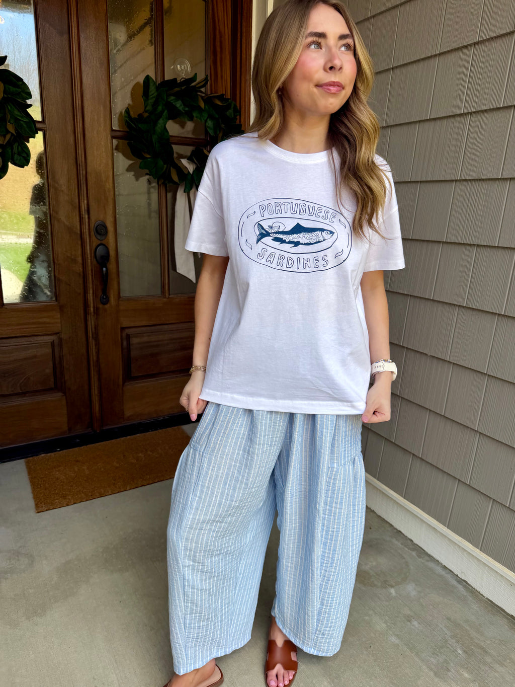 Woman wearing a white t-shirt with a graphic design and light blue pants standing outside a house.
