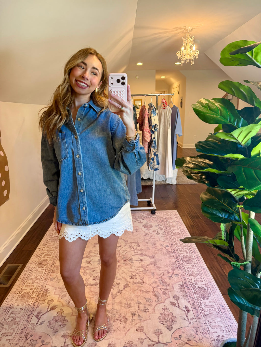 Woman taking a mirror selfie wearing a denim shirt and white lace shorts in a store.