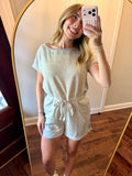 Woman taking a mirror selfie wearing a light gray romper.