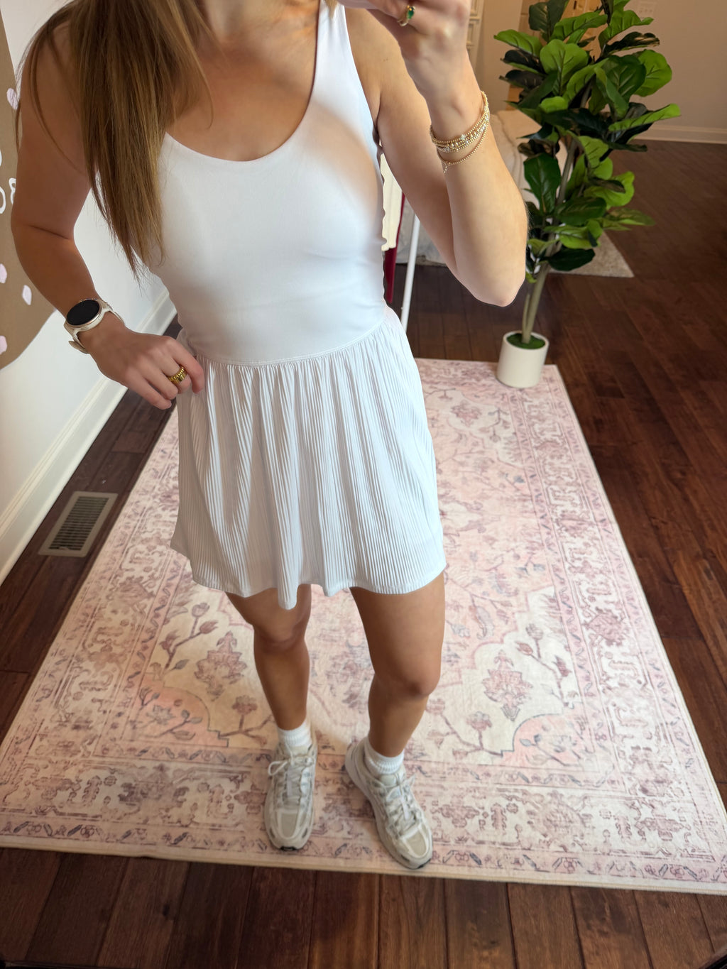 Woman in a white dress standing on a patterned rug with a plant in the background