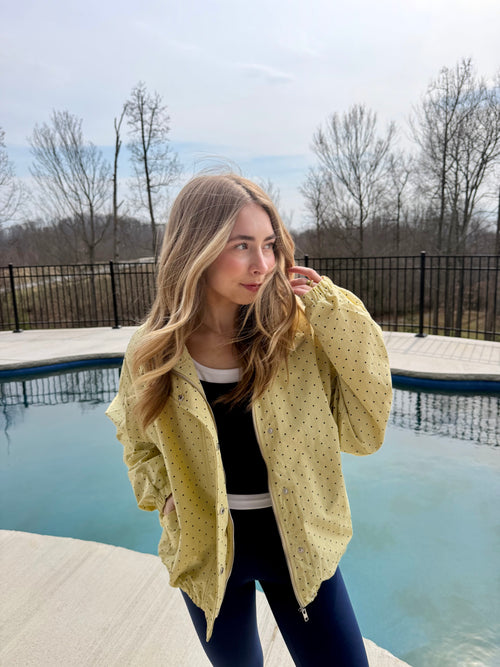 Woman in a yellow jacket standing by a pool with bare trees in the background