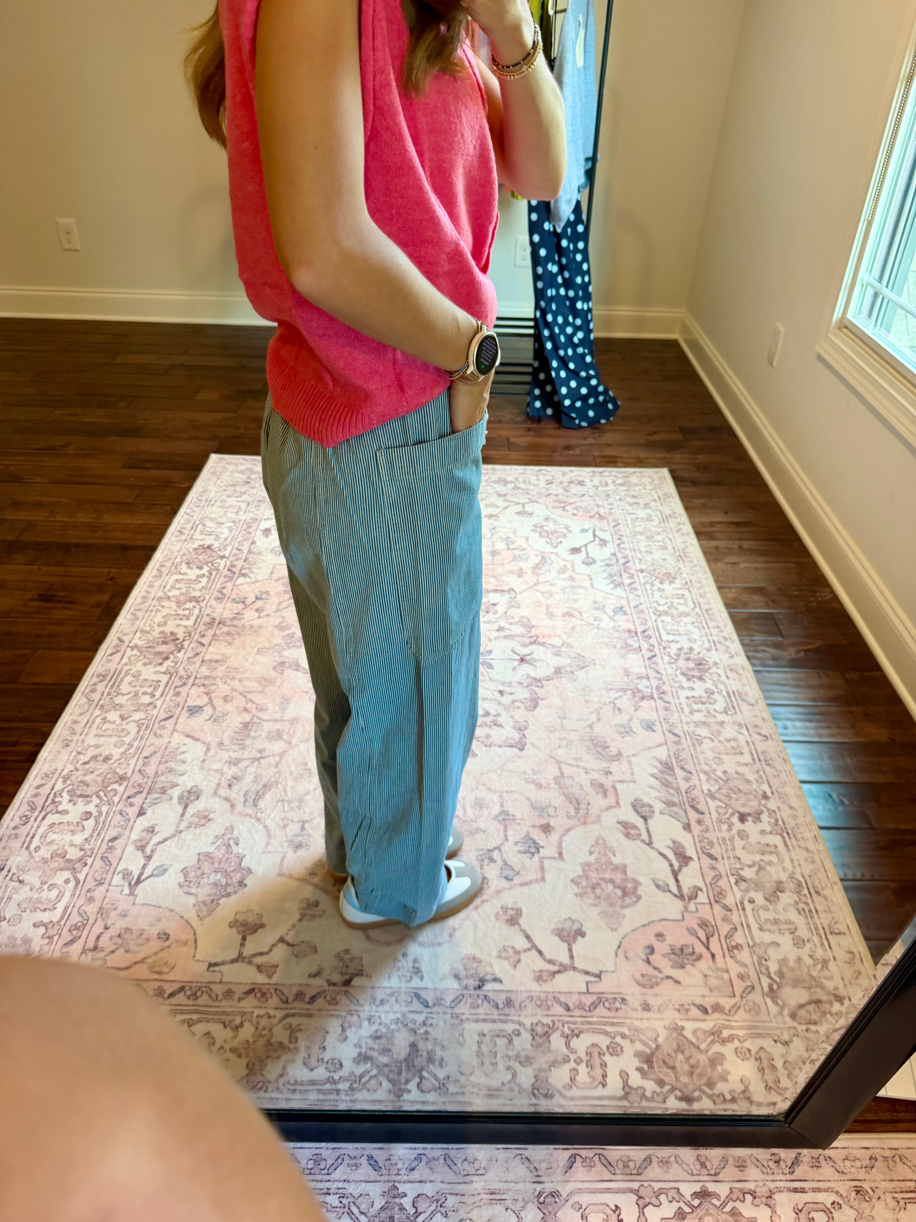 A person standing in a room wearing a bright pink sleeveless top and light blue wide-leg pants, photographed in a mirror showing a full-length view of the outfit.