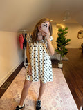 Woman in a polka dot dress standing in a room with a plant and patterned rug.