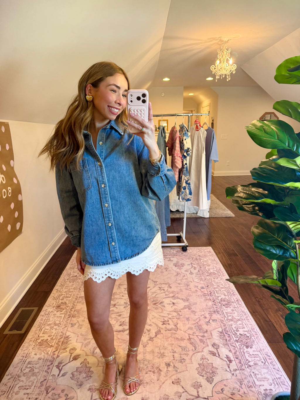 Woman taking a mirror selfie wearing a denim shirt and white lace shorts in a store.