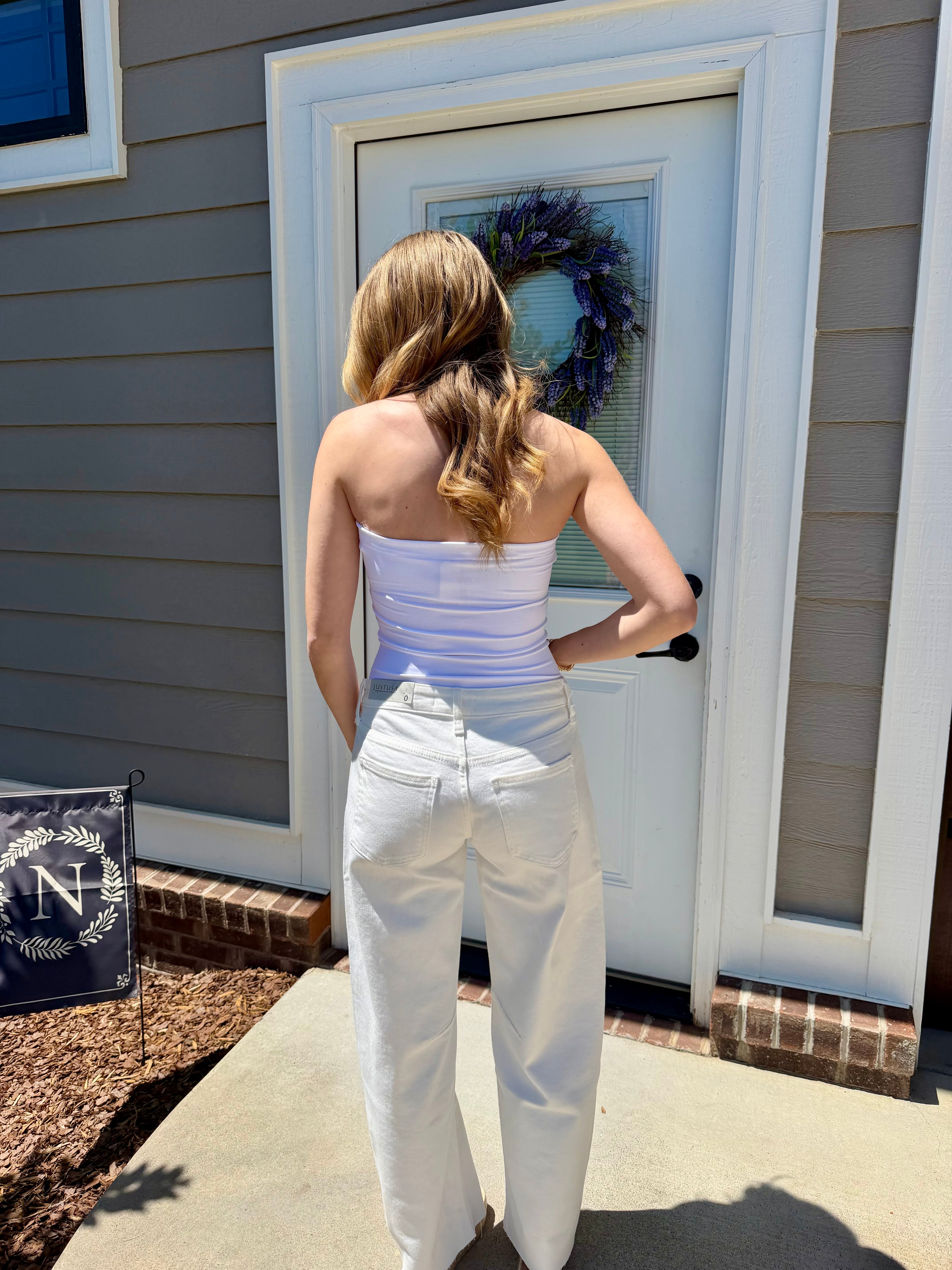 Woman in a white outfit standing outside a house with a wreath on the door.