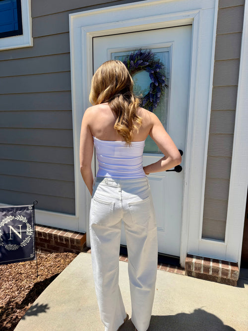 Woman in a white outfit standing outside a house with a wreath on the door.